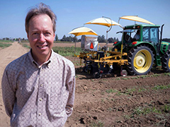 Photo: David Slaughter, professor of biological and agricultural engineering at UC Davis, in farm field with robotic tractor behind him