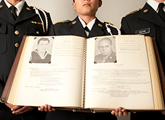 Photo: Army ROTC cadets, faces obscured, hold Golden Memory Book, showing two pages for Aggies lost in war